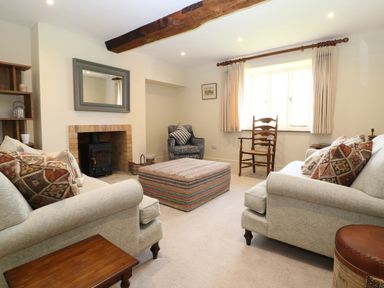 A living room with two sofas, an armchair, a wooden chair, a large ottoman, and a wood-burning stove at Morgans Farmhouse in Bampton Oxfordshire