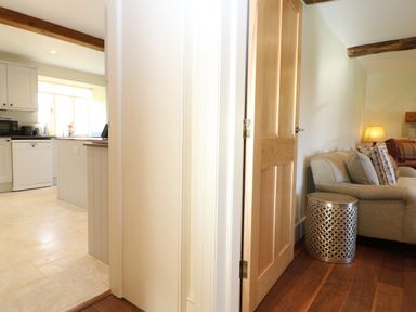 A view showing part of a kitchen with white cabinets and a dishwasher and a living area with a sofa and a metallic side table at Morgans Farmhouse in Bampton Oxfordshire