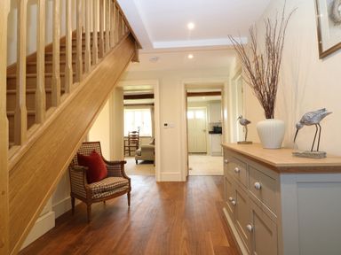 A hallway with a wooden staircase a patterned armchair and a cabinet with decorative items at Morgans Farmhouse in Bampton Oxfordshire