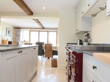 A kitchen with a red stove island cabinetry and dining table with chairs at Morgans Farmhouse in Bampton Oxfordshire