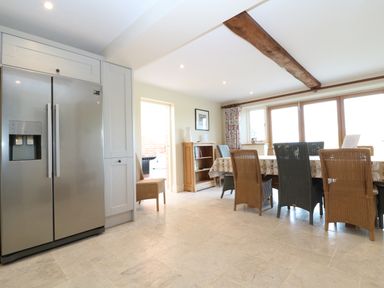 A kitchen dining area with a stainless steel refrigerator wooden chairs and a wooden bookshelf at Morgans Farmhouse in Bampton Oxfordshire
