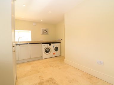 A utility room with washing machine and dryer under countertop with cabinets and a small window at Morgans Farmhouse in Bampton Oxfordshire