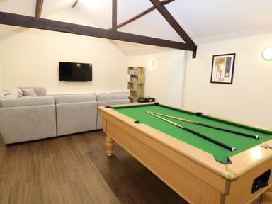 A game room with a pool table, gray sectional sofa, wall-mounted TV, shelf with DVDs, and framed picture on the wall at Morgans Farmhouse in Bampton Oxfordshire