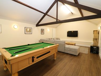 A recreational room with a pool table a gray sectional sofa a wall-mounted TV and exposed wooden ceiling beams at Morgans Farmhouse in Bampton Oxfordshire