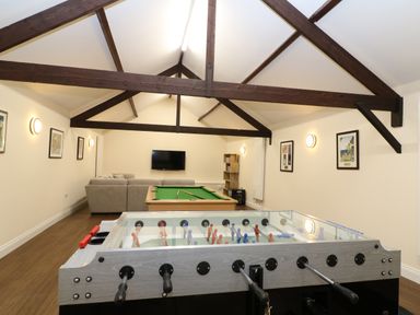 A games room with a foosball table pool table sofa wall-mounted tv and wooden beams on the ceiling at Morgans Farmhouse in Bampton Oxfordshire