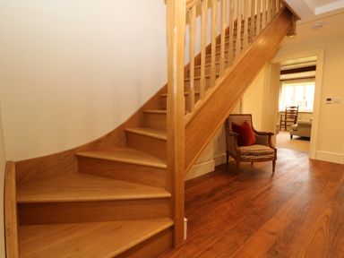 A wooden staircase with a checkered armchair and a red pillow on a wooden floor at Morgans Farmhouse in Bampton Oxfordshire