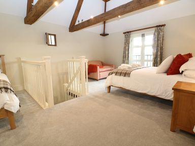 An upstairs bedroom with a bed sofa stair railing and wooden beams at Morgans Farmhouse in Bampton Oxfordshire