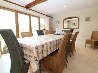 A dining room with a large table covered with a patterned tablecloth and wicker chairs at Morgans Farmhouse in Bampton Oxfordshire