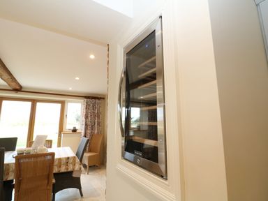 A dining area with a table set for tea and wicker chairs near a built in wine fridge at Morgans Farmhouse in Bampton Oxfordshire