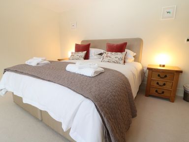A bedroom with a bed with red and floral cushions a brown quilted bedspread two folded towels on the bed two wooden bedside tables with lit lamps Morgans Farmhouse Bampton Oxfordshire