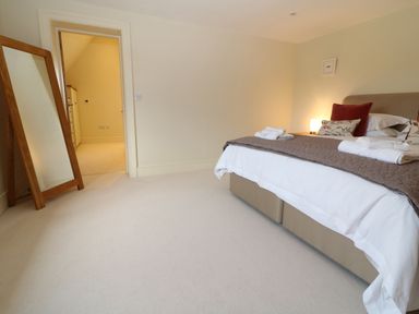 A bedroom with a bed with pillows and towels a wooden floor mirror and an open door showing a hallway at Morgans Farmhouse in Bampton Oxfordshire