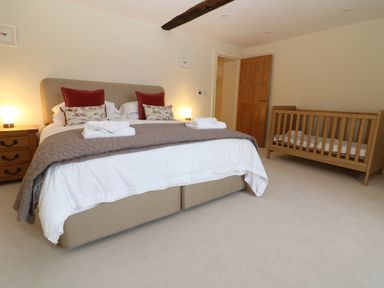 A bedroom with a double bed wooden crib bedside table and open door at Morgans Farmhouse in Bampton Oxfordshire