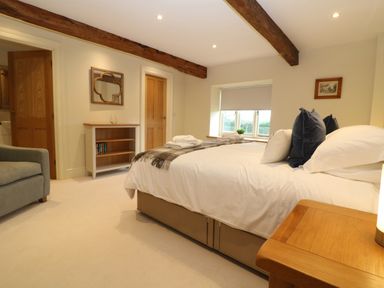 A bedroom with a bed decorated with pillows and folded towels a small bookshelf a framed mirror and wooden beams on the ceiling at Morgans Farmhouse in Bampton Oxfordshire