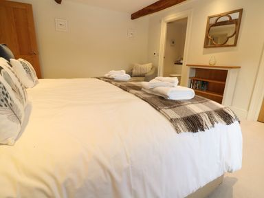 A bedroom with a large bed with pillows and folded towels a gray armchair a wooden door a shelving unit with books and a mirror on the wall at Morgans Farmhouse in Bampton Oxfordshire