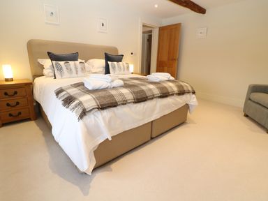 A bedroom with a double bed two bedside tables with lamps a wooden door and a grey armchair at Morgans Farmhouse in Bampton Oxfordshire