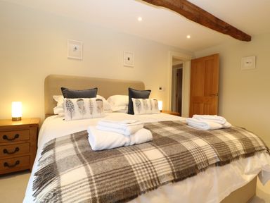 A bedroom with a large bed covered with a plaid blanket and pillows beside wooden nightstands at Morgans Farmhouse in Bampton Oxfordshire