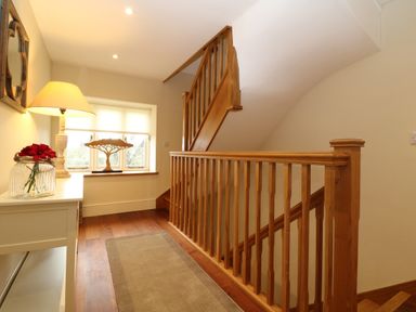 A hallway with wooden staircase railing lamp on white table and decorative tree sculpture on window sill at Morgans Farmhouse in Bampton Oxfordshire
