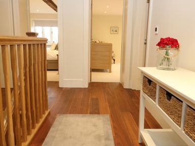 A hallway with wooden flooring a beige rug and a white console table with baskets and red flowers at Morgans Farmhouse in Bampton Oxfordshire