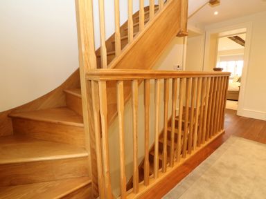 A wooden staircase with balusters leading to an upstairs hallway with a room visible at the end at Morgans Farmhouse in Bampton Oxfordshire
