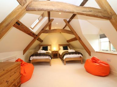 An attic bedroom with two single beds a wooden nightstand between them and orange bean bags at Morgans Farmhouse in Bampton Oxfordshire