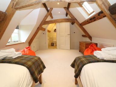 A bedroom with two single beds under exposed wooden beams and a doorway leading to a bathroom at Morgans Farmhouse Bampton Oxfordshire