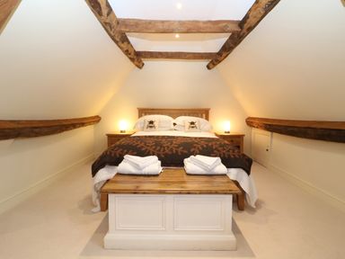 A bedroom with a double bed two bedside tables with lamps wooden beams on ceiling and folded towels on a bench at Morgans Farmhouse in Bampton Oxfordshire
