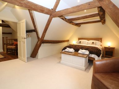 A bedroom with wooden beams on the ceiling a bed with bedside tables and lamps a chest at the foot of the bed and a leather armchair at Morgans Farmhouse in Bampton Oxfordshire