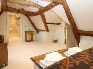 An attic bedroom with exposed wooden beams a small wooden table and an open door leading to a bathroom at Morgans Farmhouse in Bampton Oxfordshire