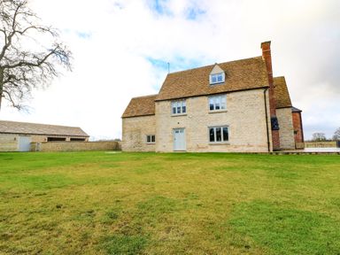 An exterior view of a stone farmhouse with a lawn and a separate stone outbuilding at Morgans Farmhouse in Bampton Oxfordshire