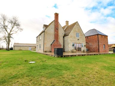 An exterior view of a stone farmhouse with a brick chimney a grassy lawn a tree and an outbuilding at Morgans Farmhouse in Bampton Oxfordshire
