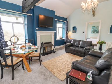 A living room with two black leather sofas a glass dining table set with plates and glasses a wall mounted tv and a fireplace at The Stable in Lydney