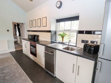 A kitchen with white cabinets black countertops a stove oven dishwasher sink and window with flowers at The Stable in Lydney