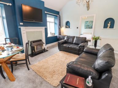 A living room with two black leather sofas a beige rug a fireplace a wall mounted tv and a glass dining table at The Stable in Lydney