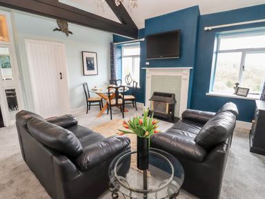 A living room with two black leather sofas a glass table with flowers a fireplace a mounted tv and a dining table with chairs at The Stable in Lydney