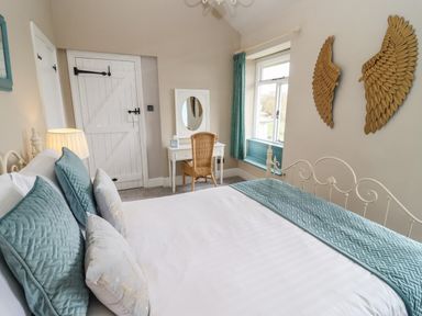 A bedroom with a bed with blue and white bedding a wicker chair a vanity table and wall decorations at The Stable in Lydney