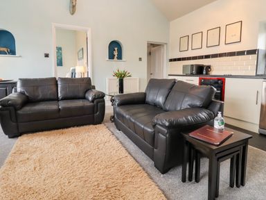 A living room with two black leather sofas a beige rug and a side table with a guest information book and hand sanitizer at The Stable in Lydney