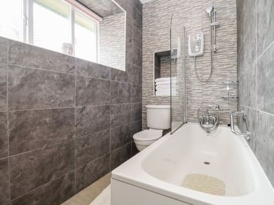 A bathroom with a bathtub shower toilet and towels at The Stable in Lydney