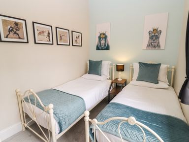 A bedroom with two single beds with blue cushions and quilts a lamp on a bedside table and animal artwork on the walls at The Stable in Lydney
