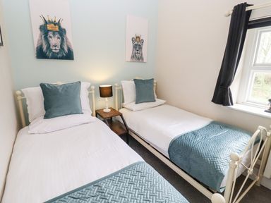 A bedroom with two single beds a bedside table with lamp and pictures of lions above the beds at The Stable in Lydney