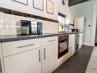 A kitchen with white cabinets a black countertop a microwave an oven a refrigerator and a window with a flower vase at The Stable in Lydney