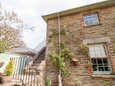 An outdoor stone staircase next to a brick building with two windows and climbing plants at The Stable in Lydney