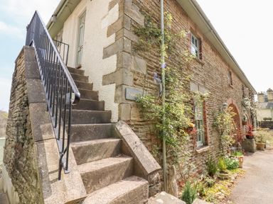 Stone staircase with black metal railing next to a stone and brick building with plants along the wall at The Stable in Lydney
