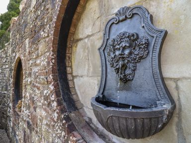 A stone wall with an arched inset featuring a decorative metal water fountain with a face at The Stable in Lydney