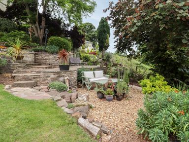 A terraced garden with stone steps a green bench with cushions and potted plants at The Stable in Lydney