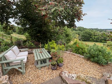 A garden seating area with a bench and table surrounded by plants and overlooking a field at The Stable in Lydney