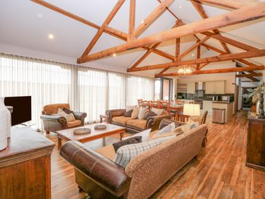 An open living and dining area with wooden beams on the ceiling sofas and a dining table at Shorthorn Barn in Attlebridge near Taverham