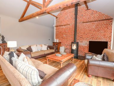 A living room with sofas and a wood burning stove against a brick wall at Shorthorn Barn in Attlebridge near Taverham