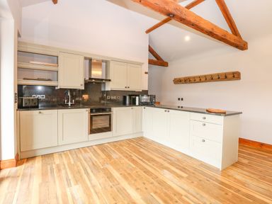 A kitchen with white cabinets black countertops wooden beams and wooden floor at Shorthorn Barn in Attlebridge near Taverham