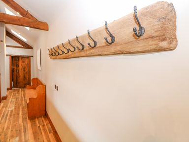 A hallway with wooden coat hooks on the wall wooden bench wooden door and exposed wooden ceiling beams at Shorthorn Barn in Attlebridge near Taverham
