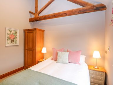 A bed with pillows and two bedside tables with lamps in a bedroom with wooden beams at Shorthorn Barn in Attlebridge near Taverham